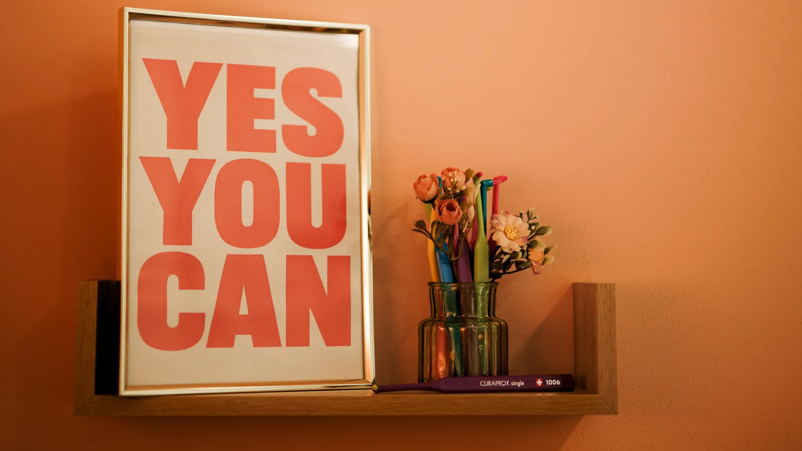 Урамљена порука Yes you can на полици у ординацији, поред вазе са четкицама за зубе